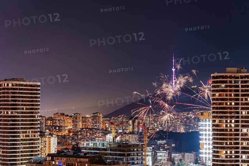 Vibrant fireworks illuminate the night sky over downtown Tbilisi, Georgia, with skyscrapers in the foreground. The festive atmosphere highlights the city's urban landscape