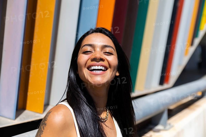 A smiling woman in a colorful outfit stands against a backdrop of vibrant modern architecture, creating a striking urban contrast that exudes energy and style