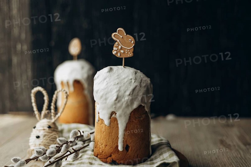 Traditional Russian kulich bread topped with white glaze and cute Easter-themed decorations, presented on a rustic wooden table for a festive celebration