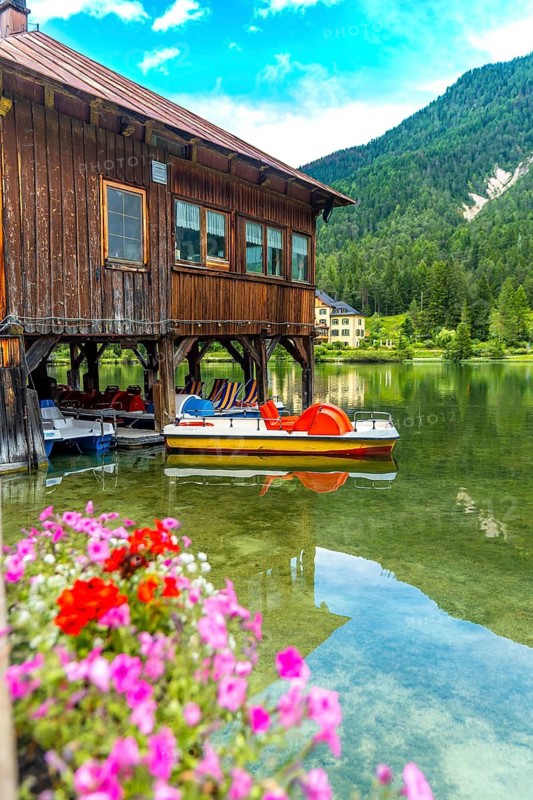 Colorful pedal boats dock under a traditional wooden boathouse on the clear waters of lake dobbiaco, framed by the stunning dolomites