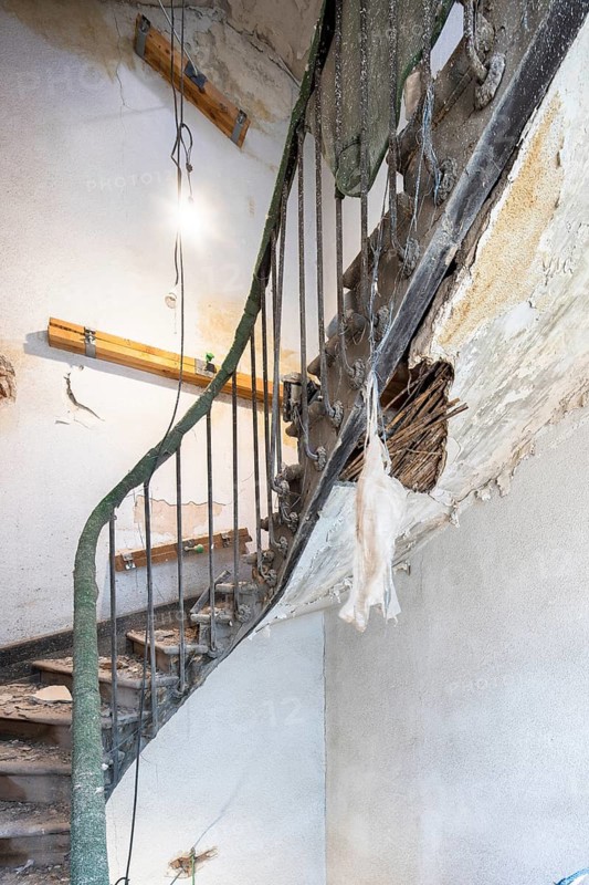 A damaged staircase in an old building undergoing renovation. Exposed areas show deterioration, while construction materials and tools indicate work in progress