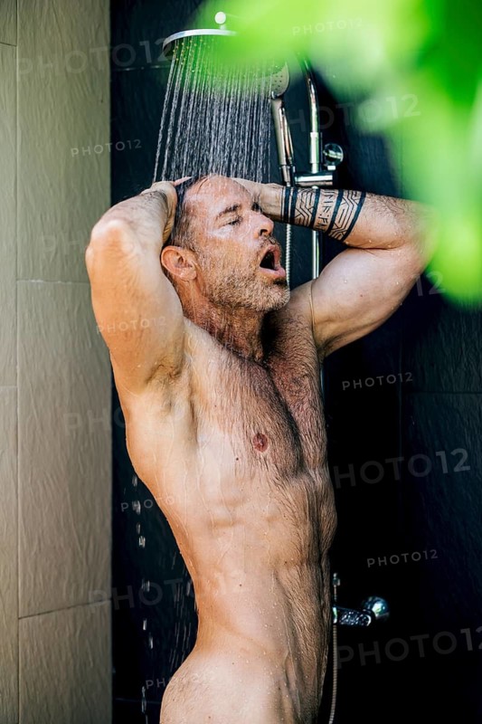 A man stands under a shower, water cascading over him, capturing a moment of refreshment and relaxation. The scene conveys a sense of tranquility and rejuvenation