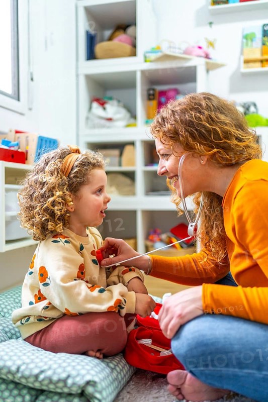 Mother listening the heartbeat of her daughter playing nurses on the floor of the bedroom