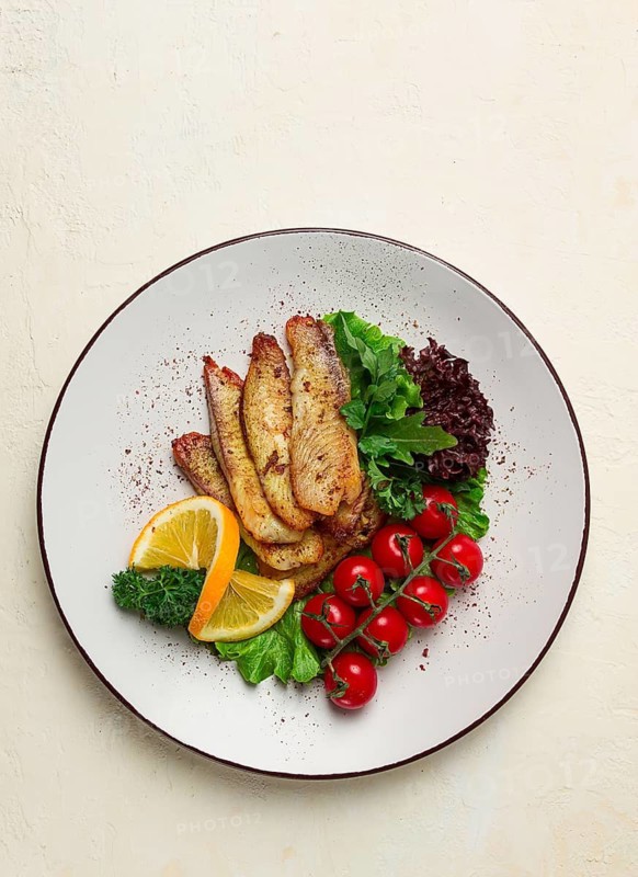 Fried Tilapia fish fillet, in spices, with cherry and salad, on a white plate, homemade, no people