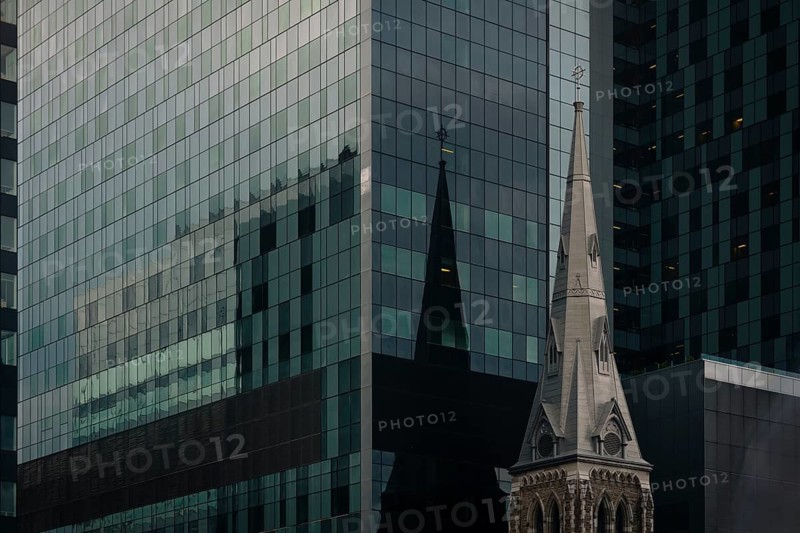A striking juxtaposition of Montreal's urban landscape featuring a modern glass skyscraper reflecting the silhouette of a historic church spire, highlighting architectural diversity