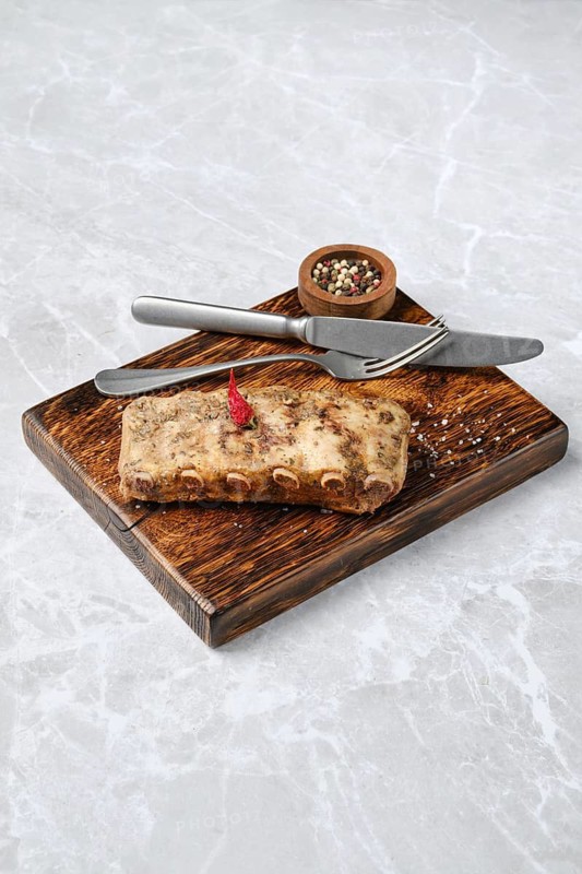 Juicy grilled ribs on a rustic wooden board, with a small bowl of mixed spices. A knife and fork are elegantly placed beside the meat, enhancing the appetizing presentation