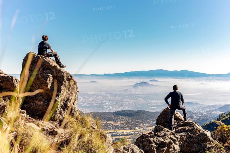 Two friends relish a scenic moment atop a mountain They admire the vast landscape, clear sky, and distant peaks, celebrating friendship and adventure in nature