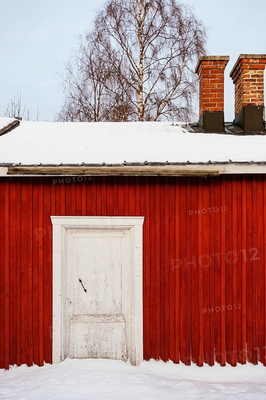 Traditional red wooden cabin against a snow-covered landscape in Swedish Lapland. The rustic architecture and serene backdrop capture the essence of Scandinavian winter