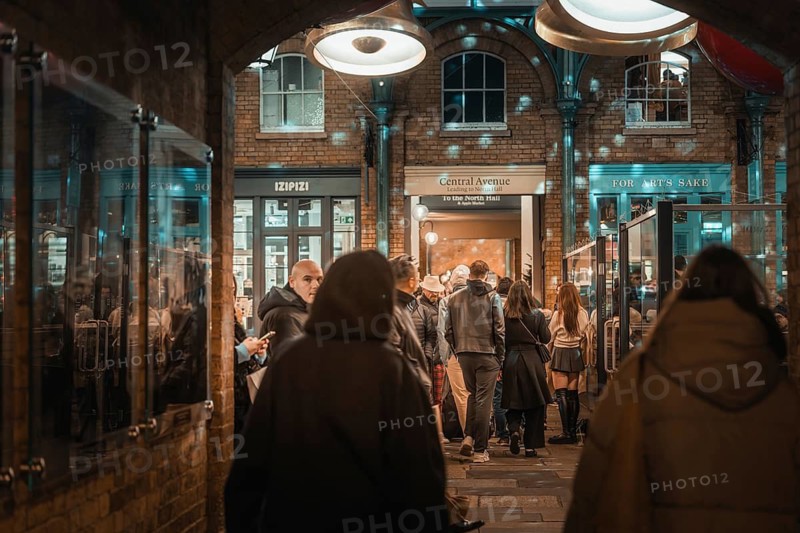 Evening view of a busy passage with people and shimmering lights above the shops, AppleMarket, London, United Kingdom