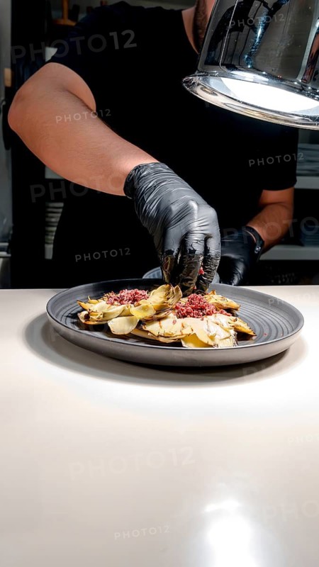 A chef expertly prepares a gourmet dish, showcasing finely chopped ingredients and culinary artistry on a dark plate. The focus is on detail and quality in plating