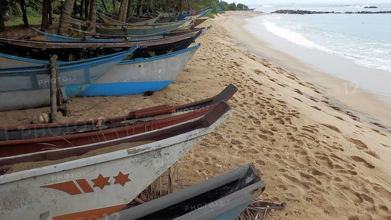 Several colorful fishing boats are moored on a sandy beach by the sea, Sri Lanka