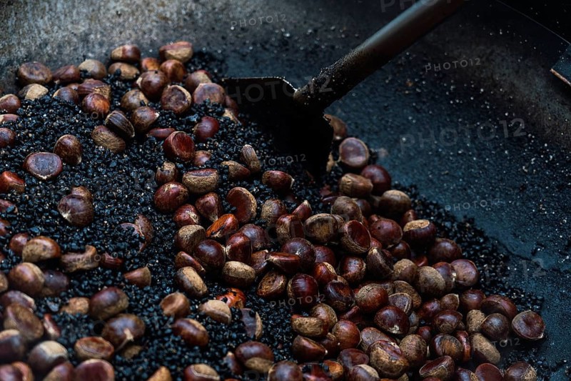 A close-up view of glistening chestnuts being roasted on a large metal pan, showcasing a traditional street food scene in Hong Kong