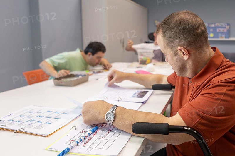 People at a day center for individuals with disabilities are engaged in activities. They are working on creative projects, highlighting a supportive environment for skill development