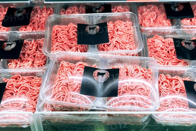Neatly packed minced meat trays are displayed on a refrigerated supermarket shelf. Each tray is wrapped in clear plastic and labeled with a cow silhouette sticker