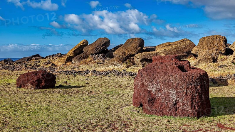 Two reddish stones in a landscape with fallen moai under cloudy sky, the moai statues on Easter Island in the Pacific Ocean