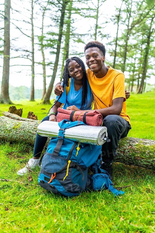 Vertical portrait of a cute young african couple embracing sitting on a log in a green beauty forest in spring