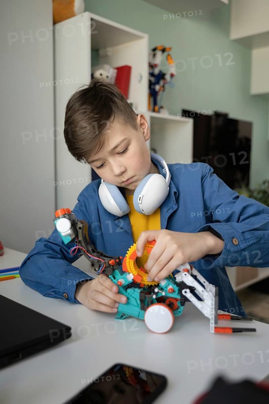 A young boy wearing headphones concentrates on assembling a colorful robot at a desk, showcasing engagement and focus in a modern home environment
