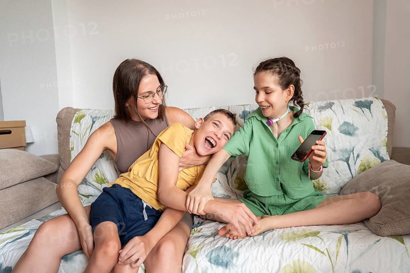 A loving family spends quality time on the couch. The girl with a tracheostomy and her brother with cerebral palsy share joyful moments, highlighting familial care and support