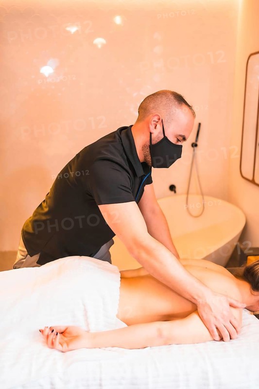 Massage at home, performing a massage at the client's home on the forearms. With a face mask in the coronavirus pandemic