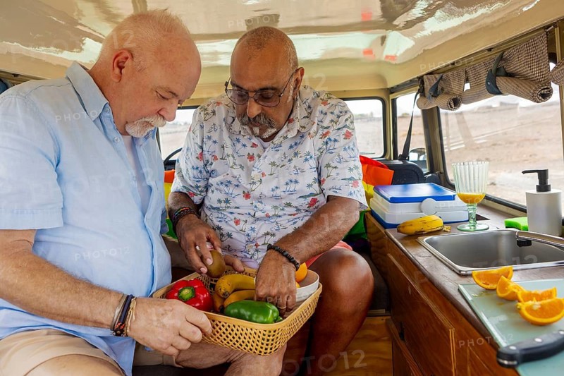 Gay senior couple enjoys preparing a fresh, colorful meal inside their off-road vehicle during a camping trip, showcasing a moment of loving partnership and domestic harmony