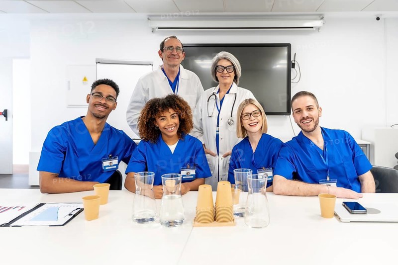 Diverse healthcare team of doctors and nurses in scrubs and white coats, smiling in a bright clinic conference room after a successful meeting about patient care and collaboration