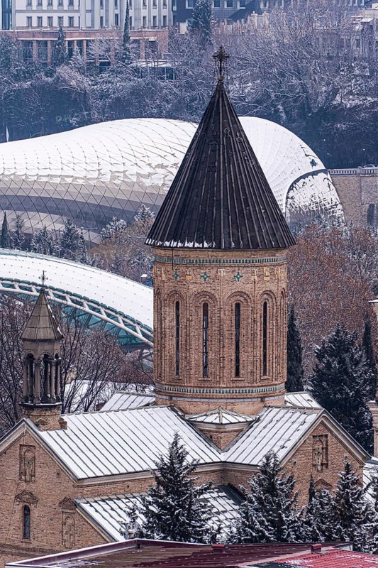 A scenic view of Tbilisi's historic center with snow-covered rooftops. The blend of ancient architecture and modern structures creates a picturesque winter scene