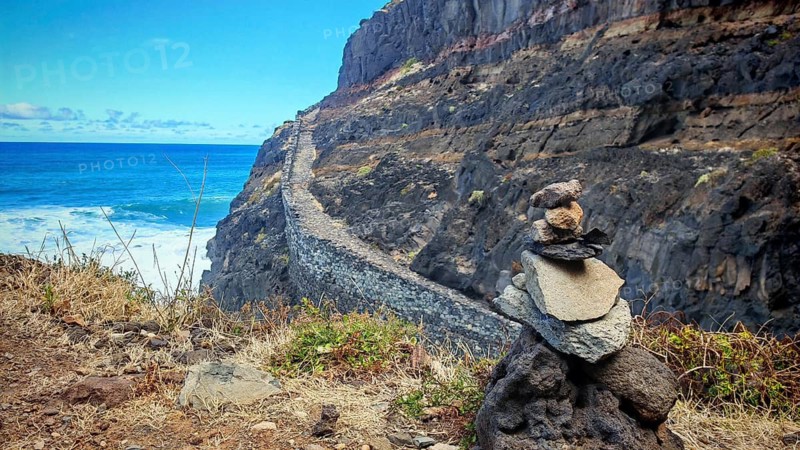 Stone tower, stone men on the edge of a cliff path with a view of the blue sea under a blue sky, hiking, Marinha da Cruzinha Natural Park, Santo Antao, Cabo Verde, Cape Verde, Cape Verde