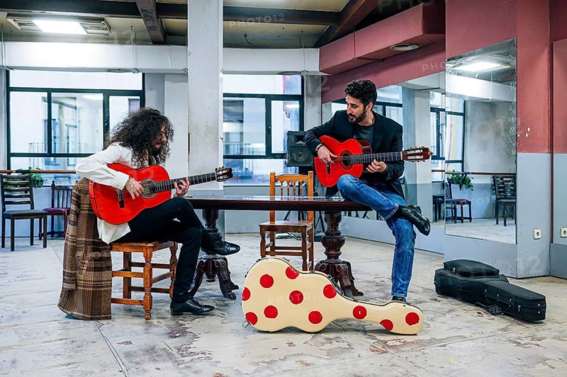 Full body of two male Latin friends playing guitars in music studio
