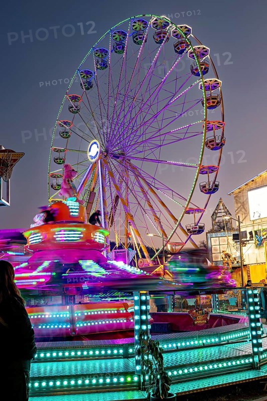 Illuminated Ferris wheel and spinning carousel at night at a fair, carousel and hustle and bustle of summer profit in Eisenach
