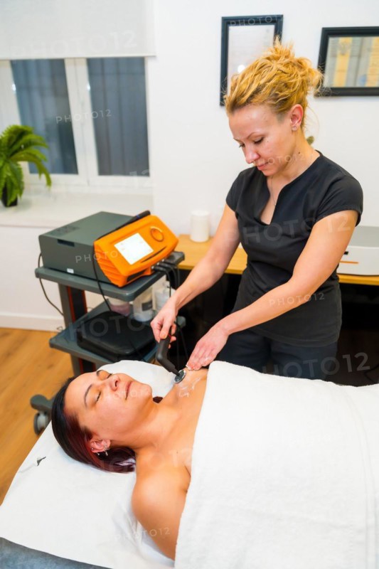 Vertical side view of a female beauty patient lying on massage table receiving indiba treatment