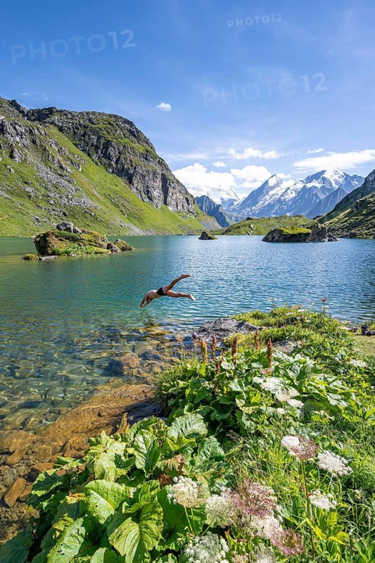 Young man, mountaineer jumping into a mountain lake with view of mountain peaks, Lac du Louvie with summit Grand Combine, Valais Alps, Val de Bagnes, Valais, Switzerland