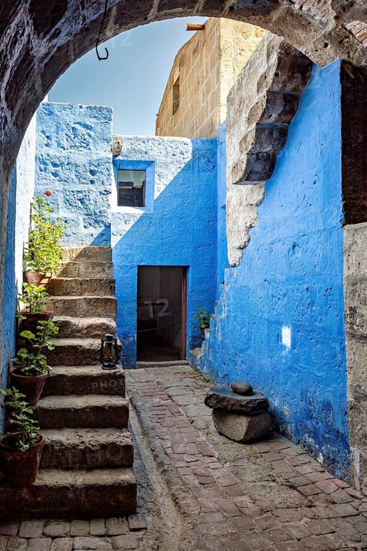 A sunny courtyard with blue walls, stone arches, stairs and lush plants that create a Mediterranean atmosphere, Santa Catalina Monastery in Arequipa in Peru