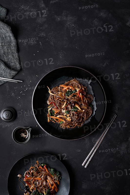 Top view chopsticks and plate with Korean dish Japchae cooked from noodles and vegetables