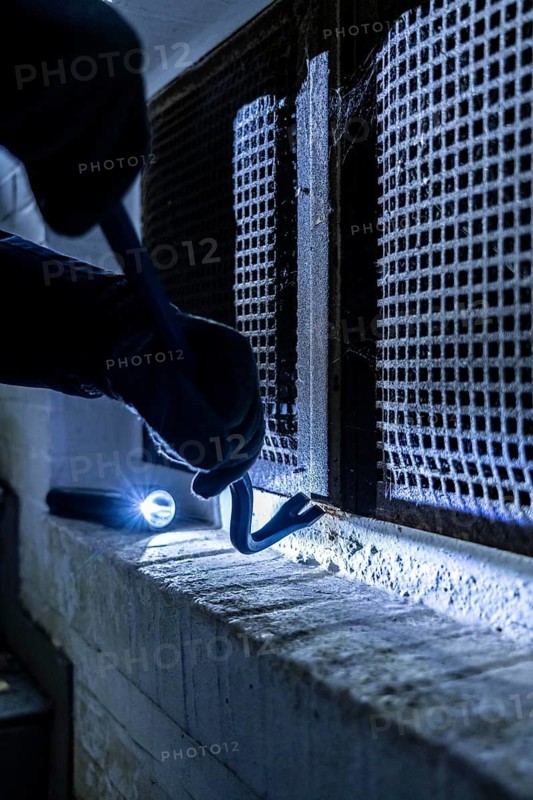 Symbolic image of a house burglary, perpetrator has approached a house from the garden side and tried to break open a cellar window to get into the flat