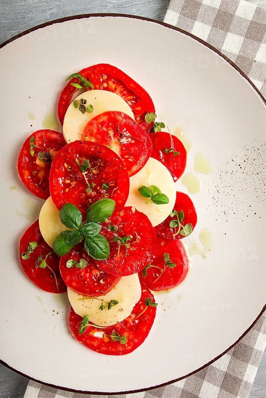 Caprese salad, Italian traditional dish, tomatoes with mozzarella cheese, basil and spices, top view, no people