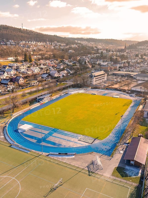 Stadium with blue running track in urban surroundings, surrounded by hills and residential houses, Nagold, Black Forest, Germany