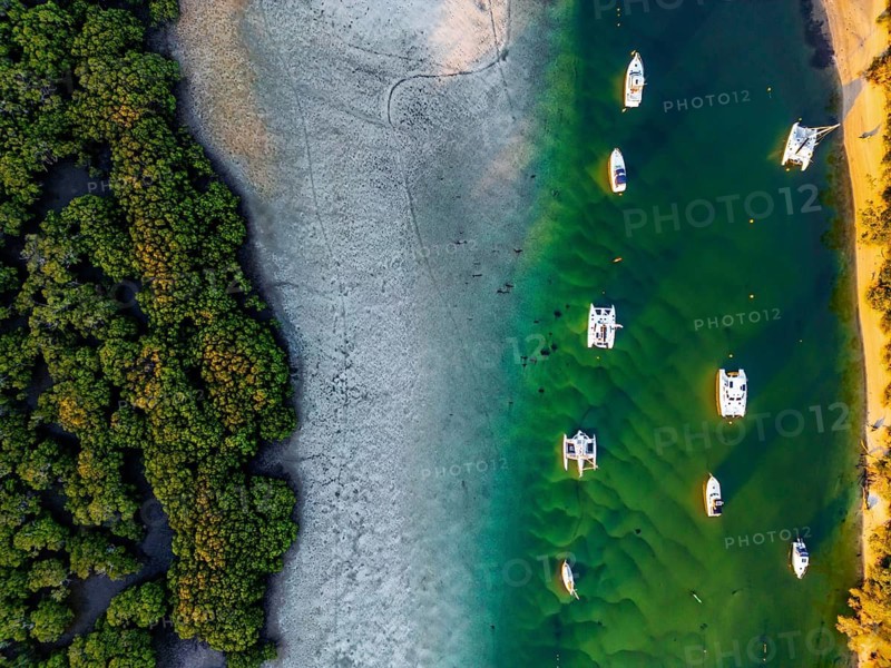 Aerial shot showcasing a tranquil coastal scene with boats anchored by vibrant green water and dense forest in Jervis Bay, Australia. Perfect harmony between nature and marine life