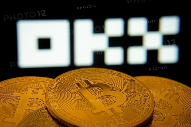 Dhaka, Bangladesh- 04 April 2025: Close-up of Bitcoin coins with the OKX logo visible on a screen in the background