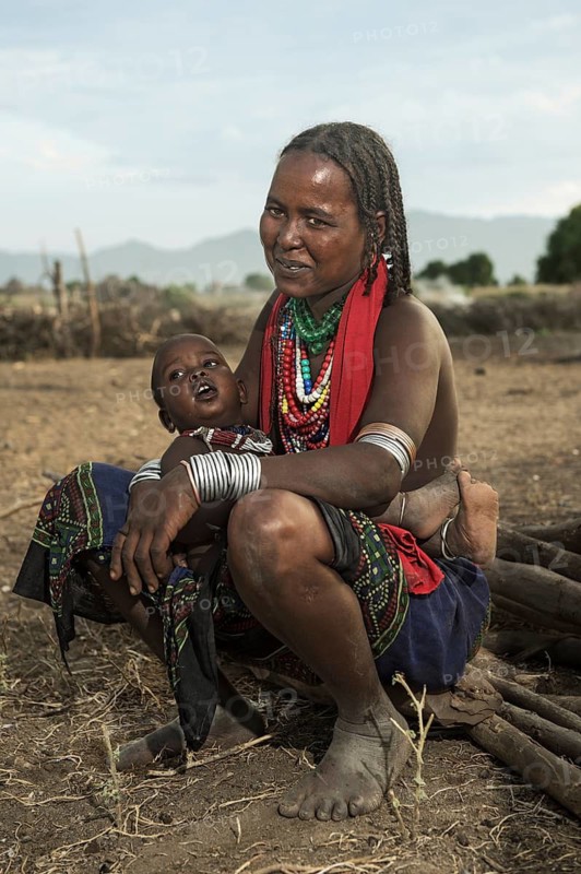 Ethnic group of the Arbore: Sitting woman with baby, wearing jewellery made of colourful bead necklaces and metal bracelets, Southern Omo Valley, Ethiopia