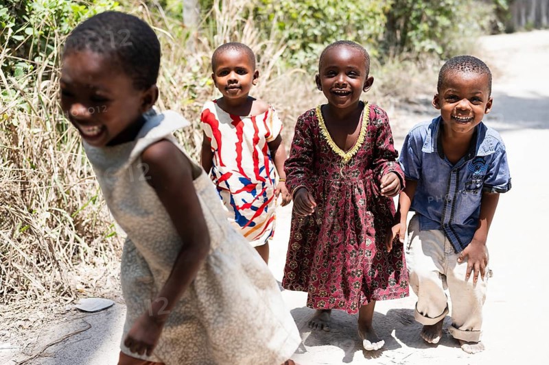 MICHAMVI KAE, ZANZIBAR - OCTOBER 17, 2025: Group of happy and laughing African children playing and running on a sunny sandy path in a rural area
