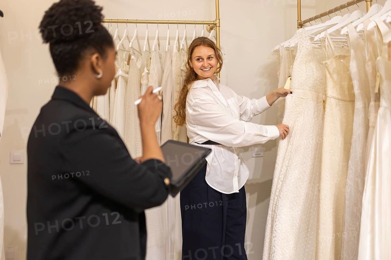 A bride to be is selecting her perfect wedding dress with the assistance of a consultant in a elegant bridal atelier, surrounded by a variety of stunning white gowns