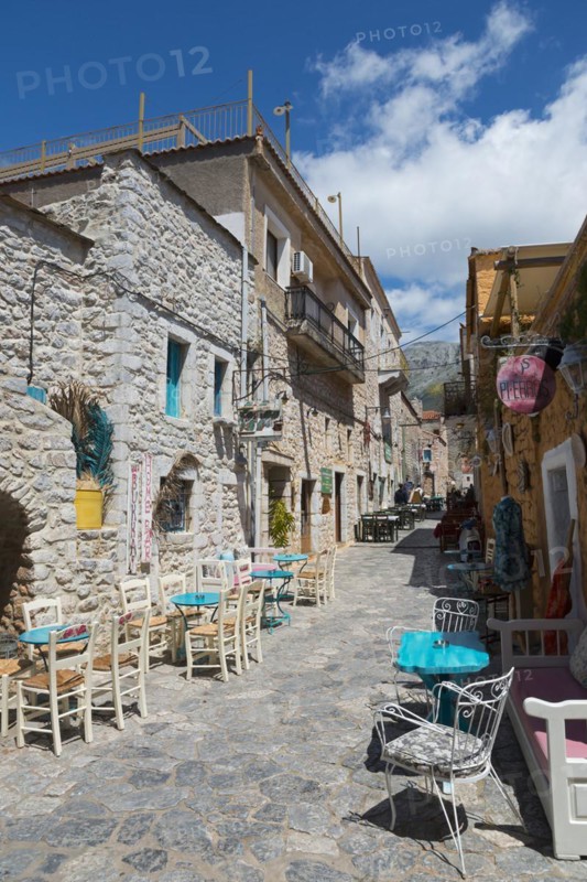 A sunny alleyway view with cafés and traditional stone buildings under a partly cloudy blue sky, alley in the old town, Areopoli, Areopolis, Tsimova, Itylo, Anatoliki Mani, Mani, Laconia, Peloponnese, Greece
