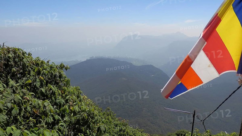 Colourful Buddhist flag fluttering in the wind over a vast mountain landscape under clear sky, view from Sri Pada, Adam's Peak, Sri Lanka