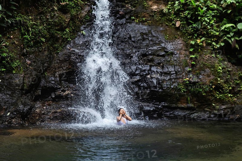 Woman enjoying a scenic waterfall in Choco Andino rainforest, Ecuador. The image captures a young Ecuadorian woman swimming in a waterfall, showcasing their connection with nature and adventure