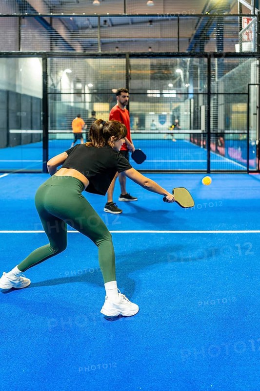 Woman striking a pickleball on a bright blue indoor court, focused and powerful in motion, showcasing fitness, agility, competitive spirit and healthy active lifestyle