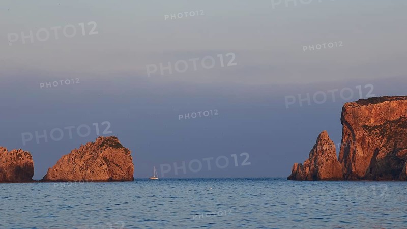 Rocky coast at sunrise with a boat in calm sea, morning light, Tsichli Babas islet, Sfaktiria island, Navarino Bay, Pylos, Peloponnese, Greece