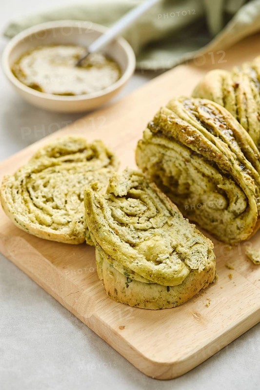 Baked homemade savoury babka plaited bread loaf flavoured with pesto on wooden bread board