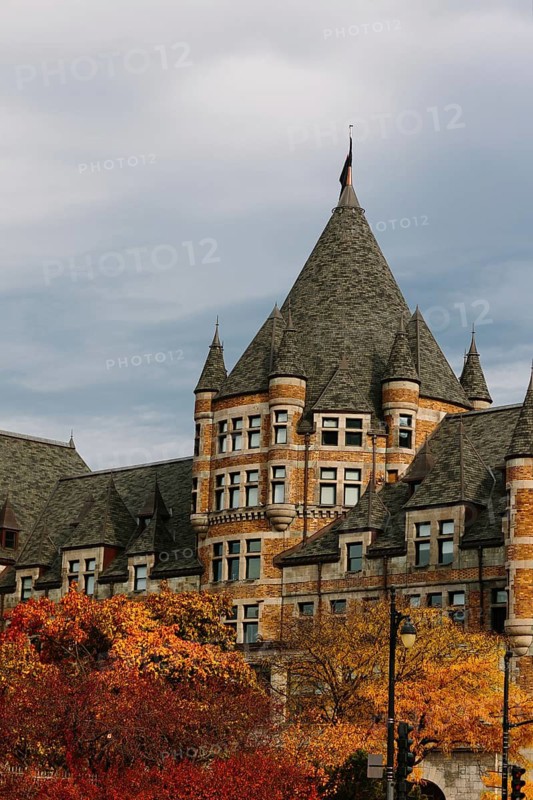A castle-like building with towering spires sits amidst vibrant fall foliage in Montreal. The structure's intricate details contrast beautifully with the fiery autumn leaves