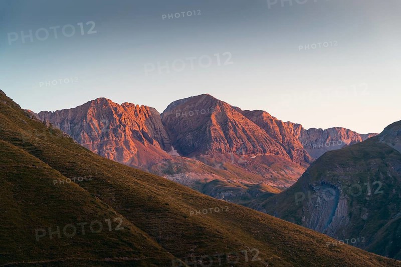 A stunning mountain range basking in the warm glow of the setting sun in summer. The play of light and shadow brings out the natural beauty of the rugged landscape in the Pyrenees