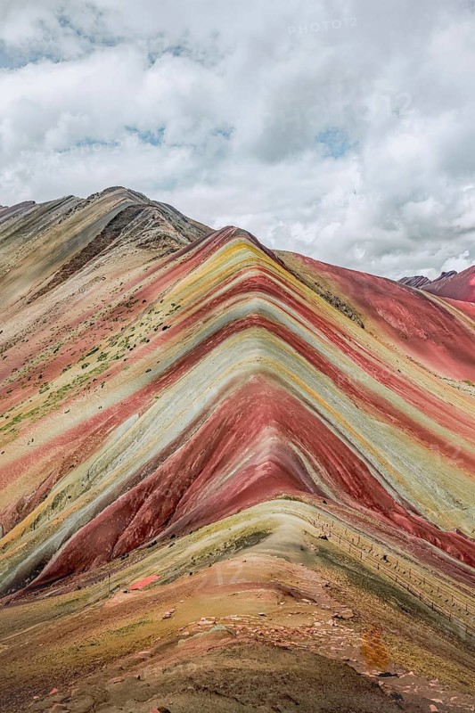 The vivid striations of Vinicunca, known as Rainbow Mountain, showcase a breathtaking view of layered mineral deposits, under a dynamic Peruvian sky